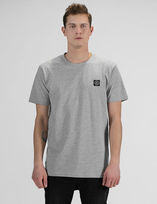 This image shows the front  pose of a young man with light brown hair, wearing a light grey Rocket Science short-sleeve t-shirt with a small square compass logo patch on the left chest.