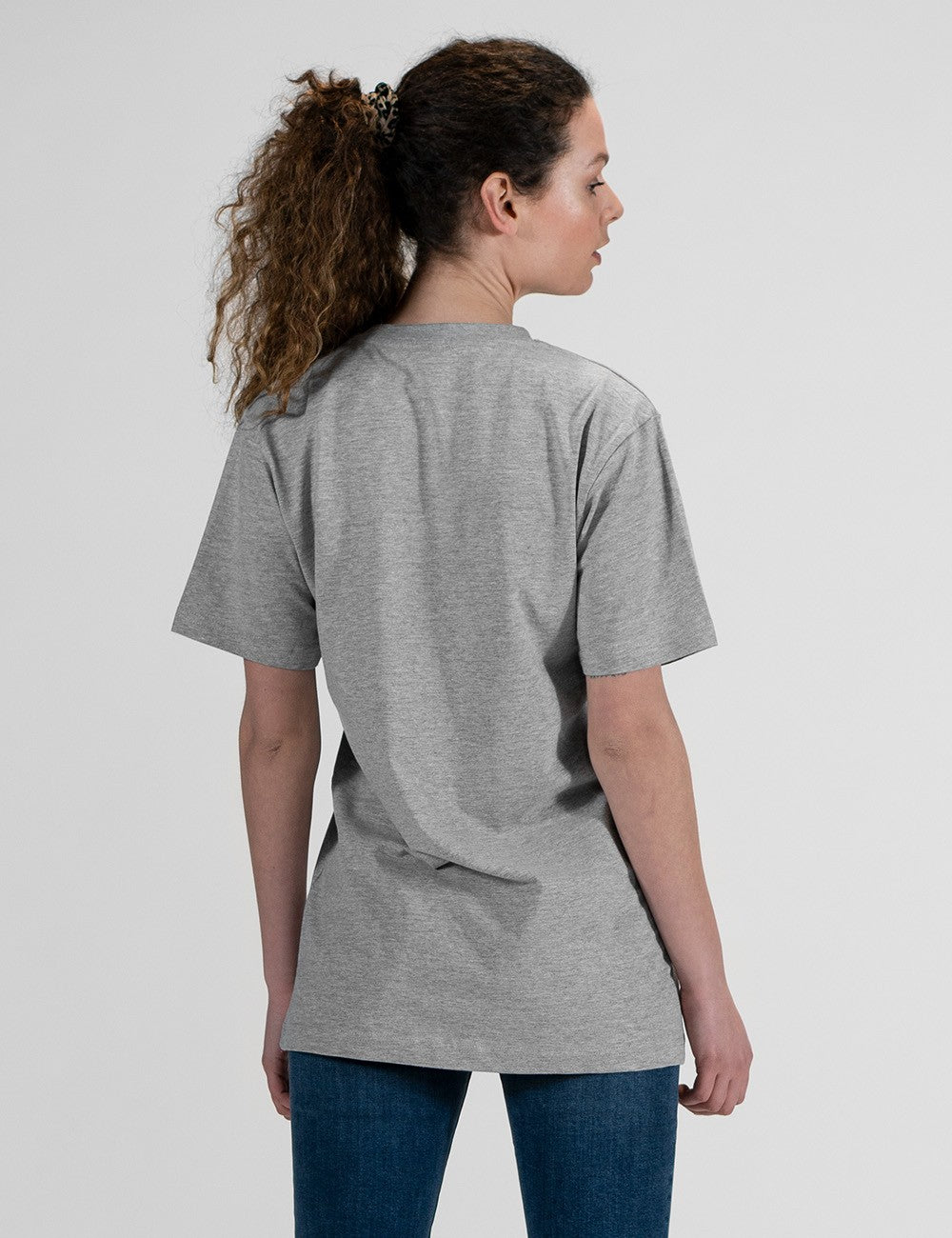 This image shows a rear pose of young woman wearing a basic heather grey crew neck t-shirt and blue jeans.