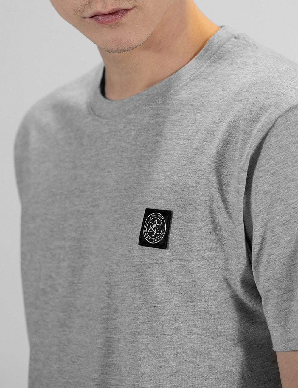 This is a grey cotton short-sleeve T-shirt featuring a small black Rocket Science logo patch on the chest.