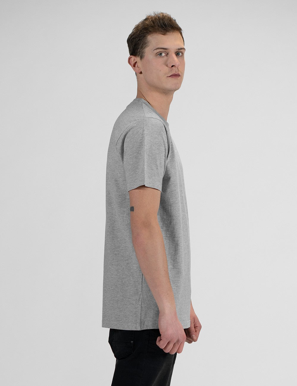 A side pose of a man wearing a casual grey crew-neck t-shirt, and dark denim jeans.