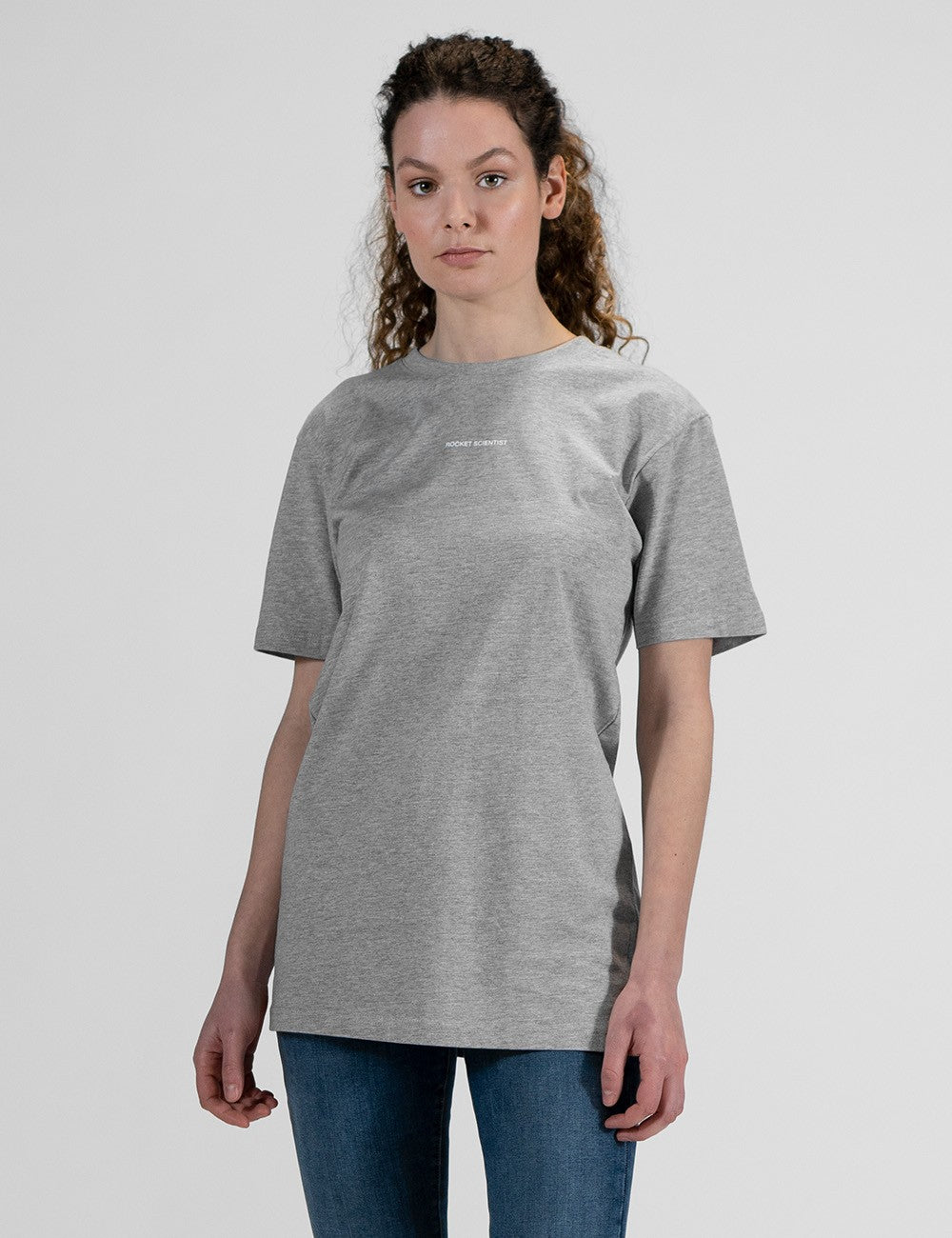 This image shows a front pose of a young woman wearing a grey crew-neck t-shirt with a print "Rocket Scientist"
, and dark blue skinny jeans.