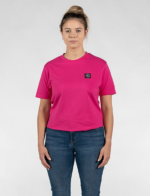 A woman modeling a bright pink short-sleeve crewneck t-shirt with a small black square Rocket Science logo patch on the left chest, paired with blue jeans, against a light gray studio background.