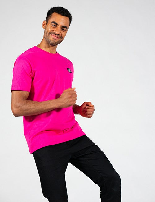 A man wearing a bright pink short-sleeve athletic t-shirt with a small black and white Rocket Science logo on the left chest, paired with black pants, posing against a light gray studio background.