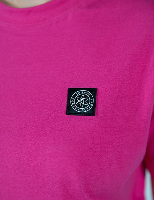 A close-up of a bright pink crewneck sweatshirt featuring a black square patch on the left chest with a white compass rose and the words 'Rocket Science' and 'EST. 2020'.