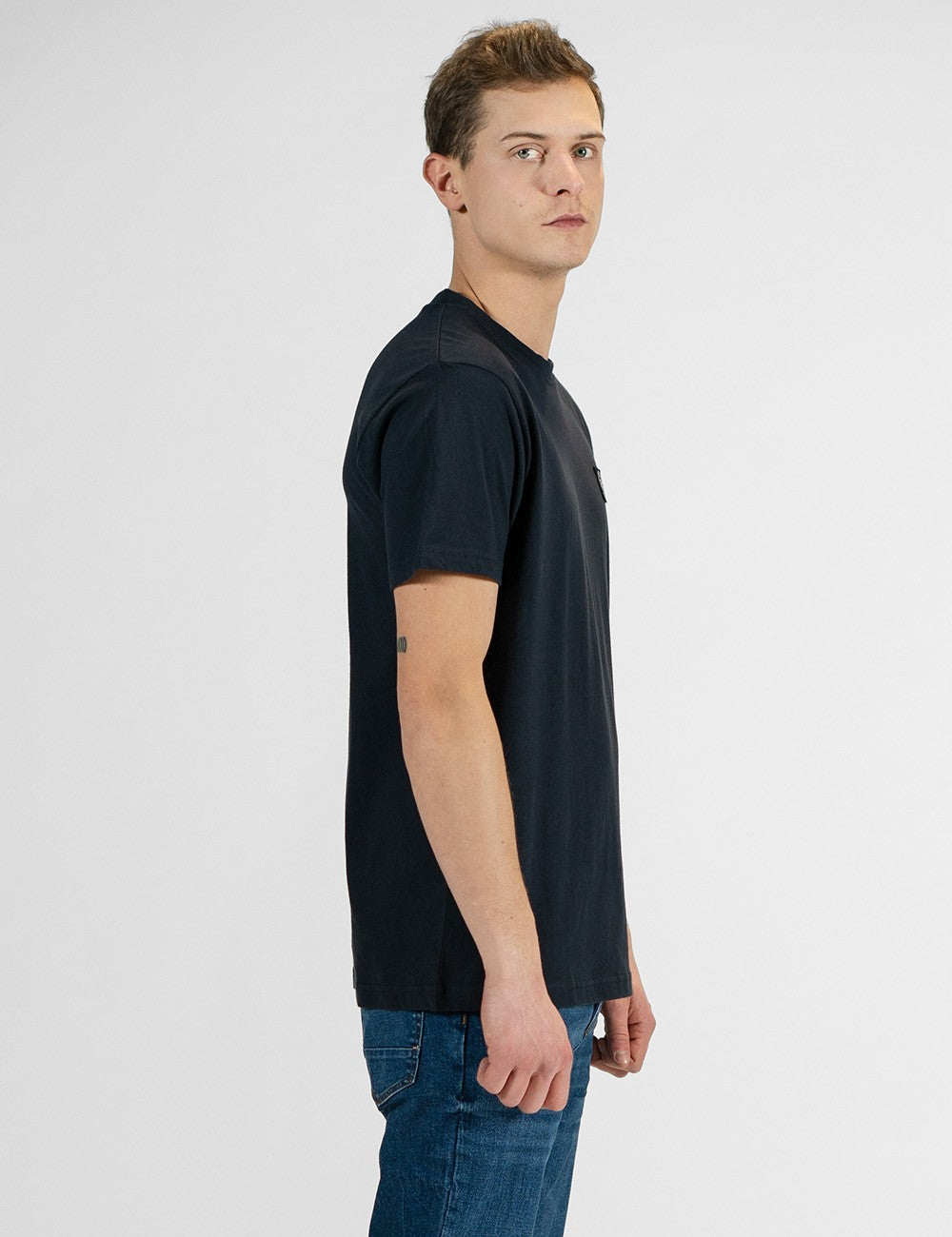 This image shows a side pose of a man wearing a classic dark navy crew-neck t-shirt paired with blue jeans.
