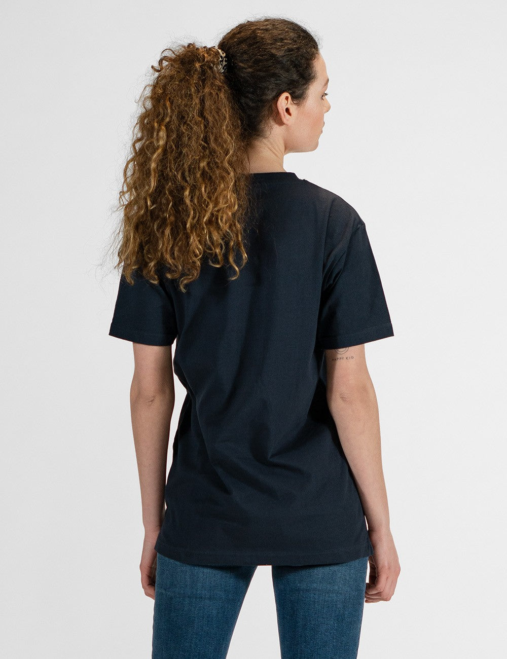 This image shows a rear pose of young woman wearing a basic navy blue short-sleeve crewneck t-shirt.