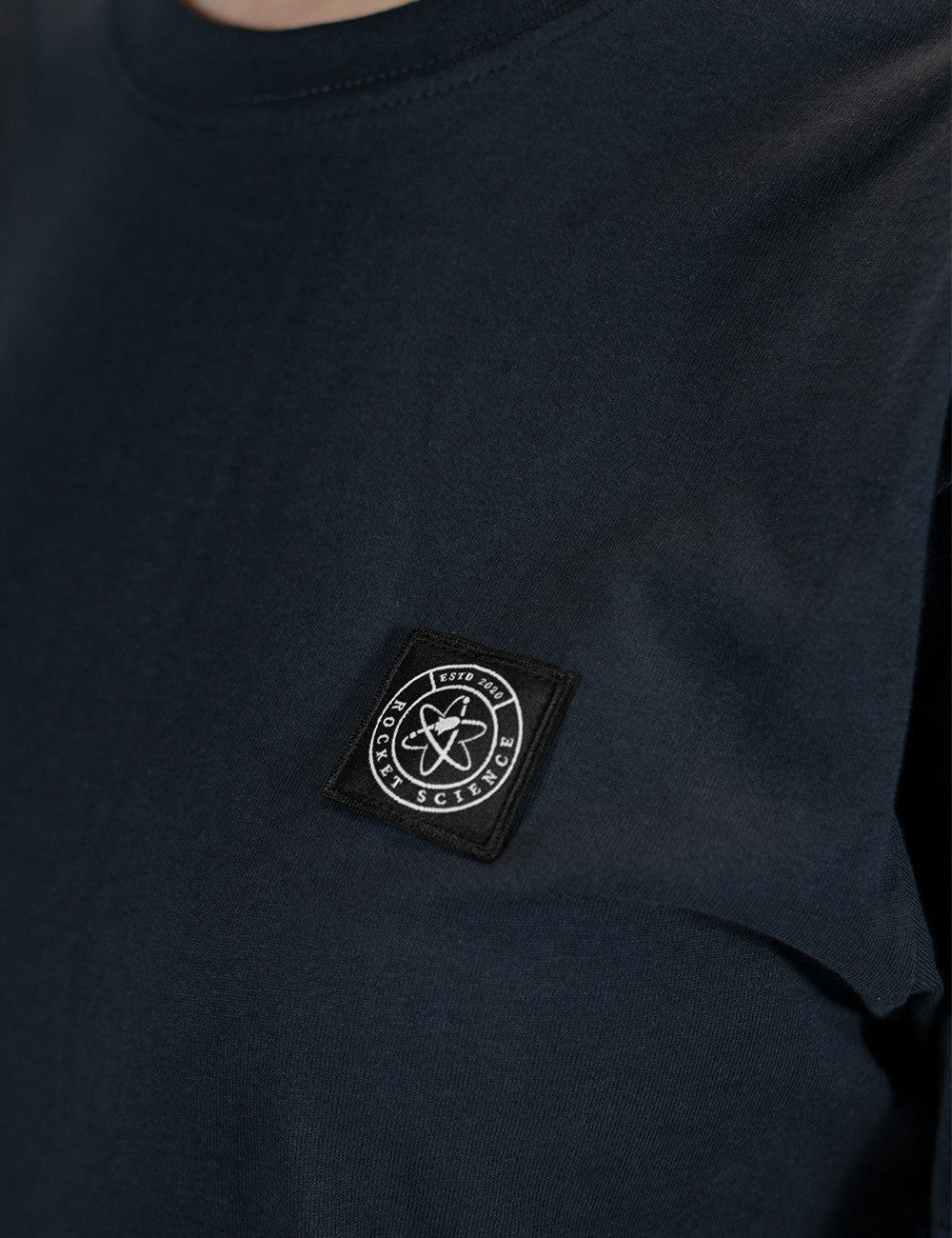This is a black cotton T-shirt featuring a square-framed circular "Rocket Science" atom logo patch on the chest.