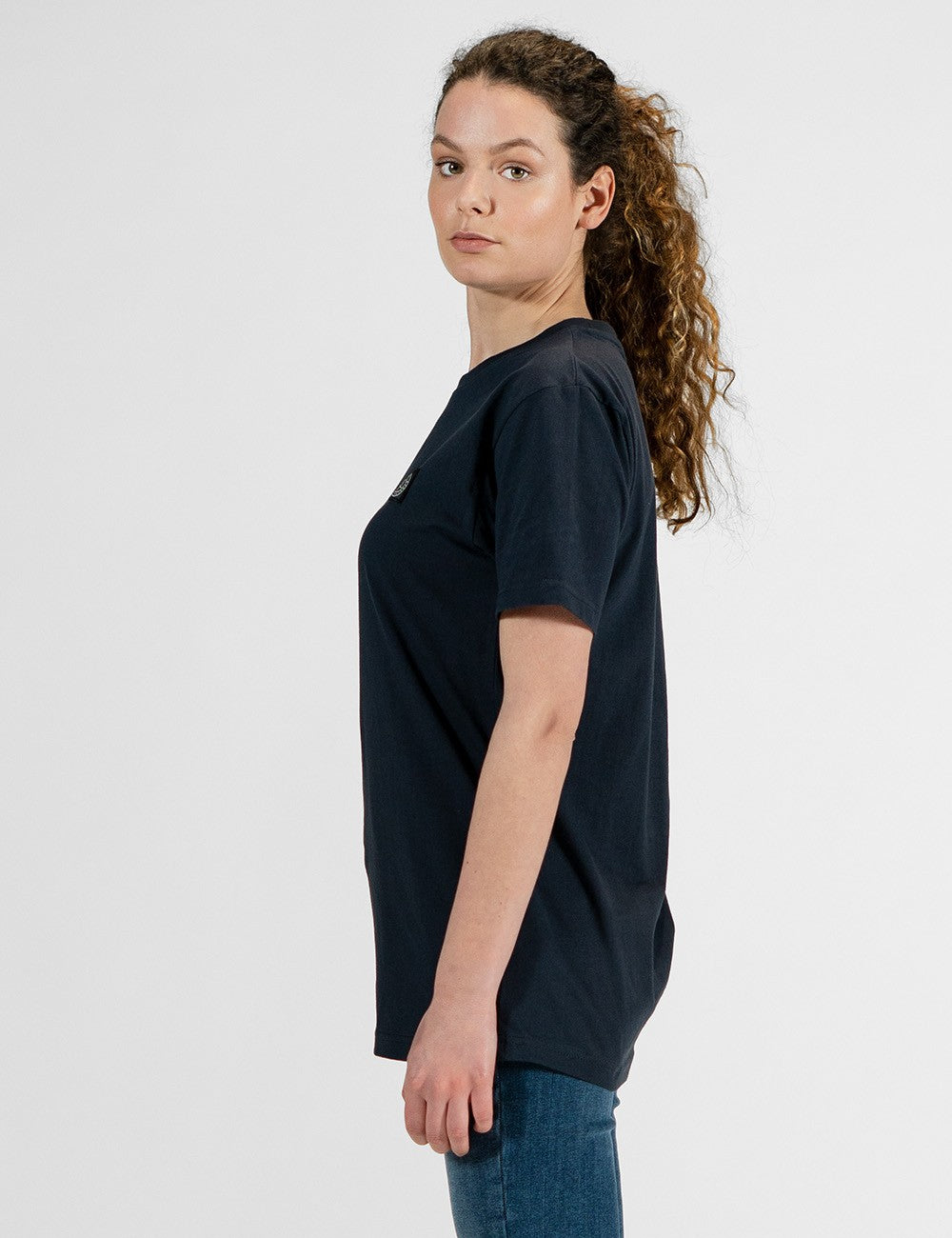  This image shows a side pose of a young woman wearing a basic navy blue short-sleeve crewneck t-shirt.