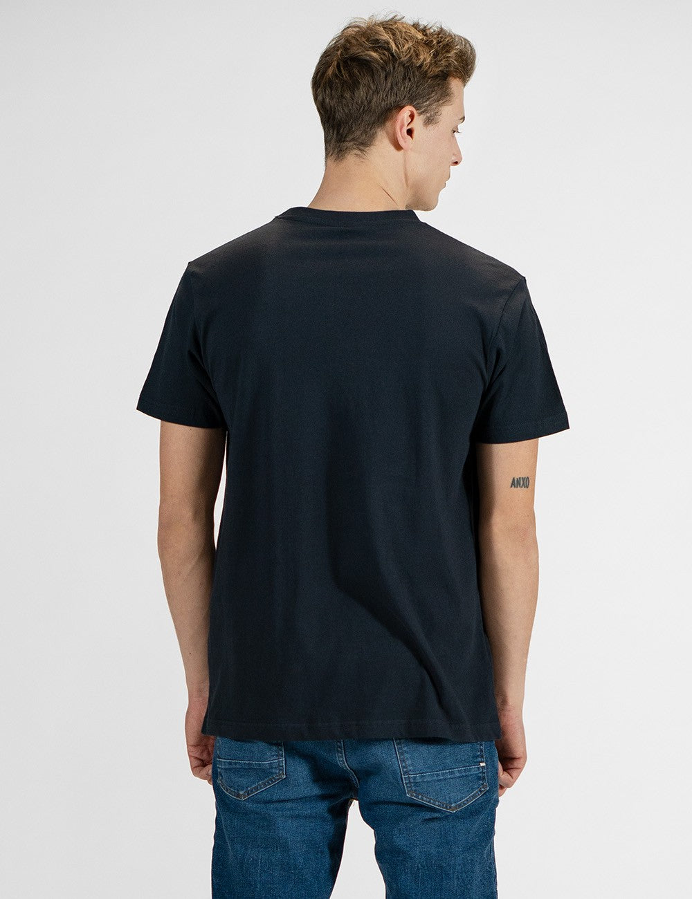 This image shows a  rear pose of a man wearing a classic dark navy crew-neck t-shirt paired with blue jeans.