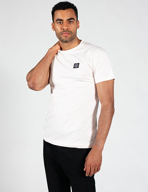A man wearing a white short-sleeve crewneck t-shirt with a small black square logo on the left chest, paired with black pants, photographed against a light gray studio background.