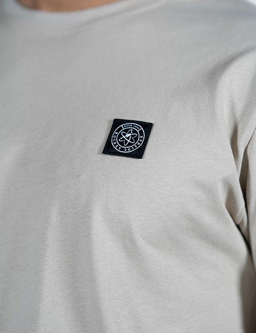 Close-up of a light gray crewneck t-shirt featuring a black square chest patch with a white circular Rocket Science logo.
