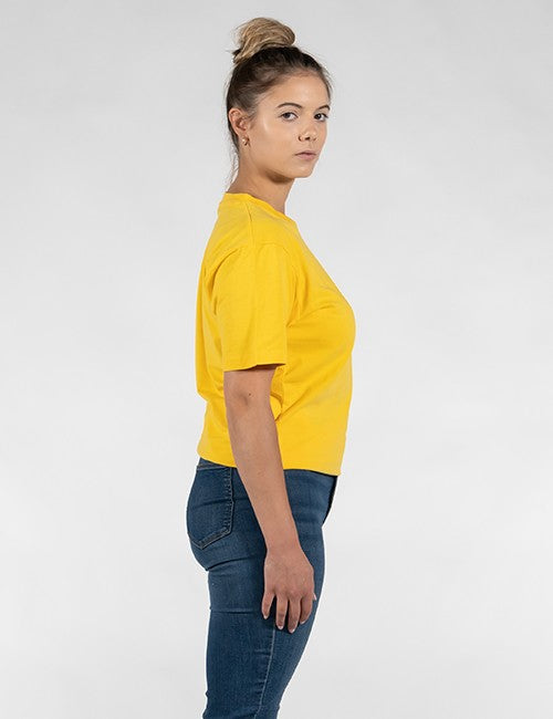 A woman shown in side profile wearing a bright yellow short-sleeve t-shirt and dark blue jeans against a light gray studio background.