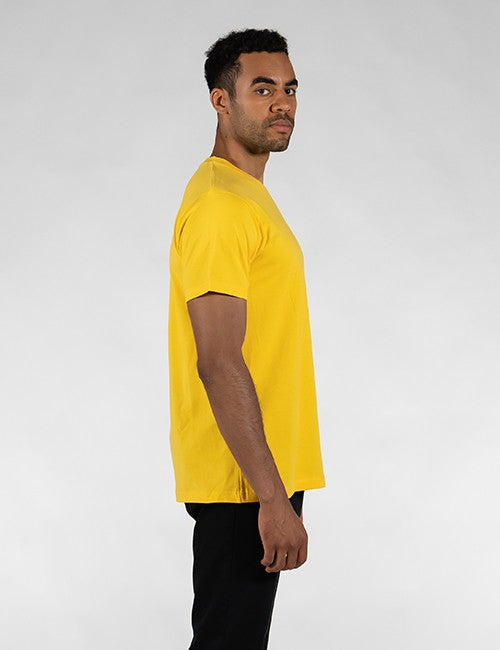 A man wearing a bright yellow short-sleeve t-shirt and black pants, shown in profile against a light gray studio background.