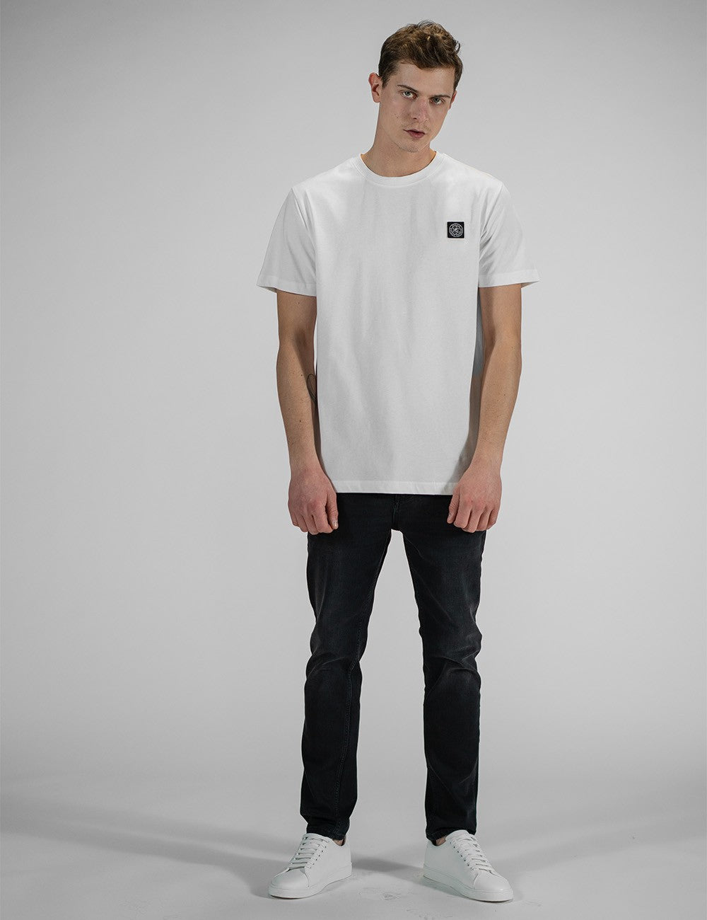 This image shows a man wearing a white Rocket Science  Cotton T-Shirt with a compass logo patch on the chest.