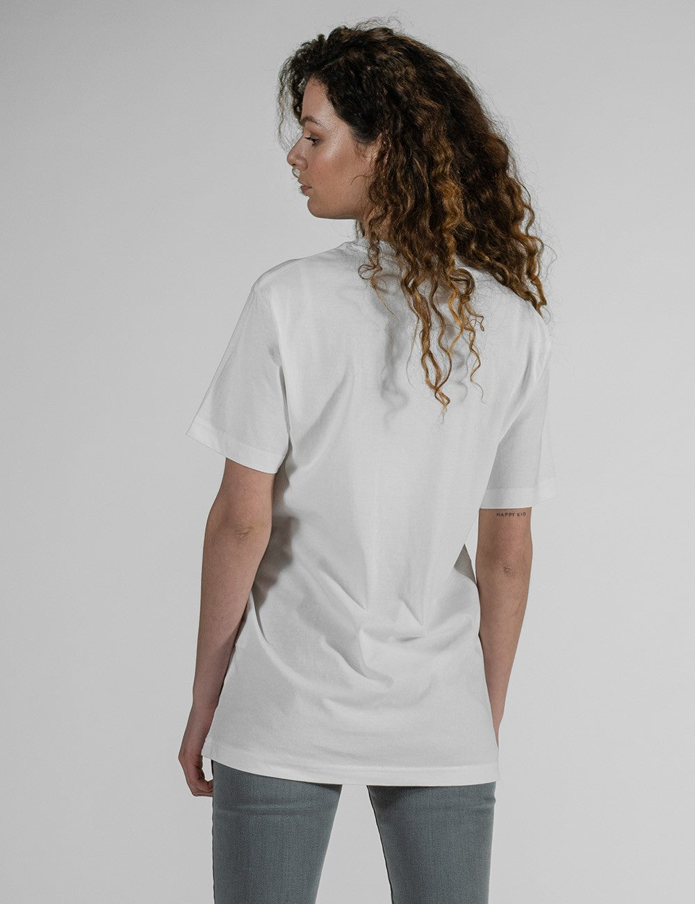 rear profile of a person with long, curly brown hair wearing an oversized plain white t-shirt and grey pants against a light grey background.